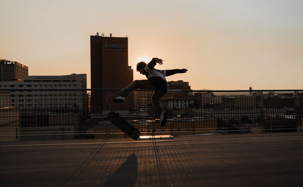 A silhouetted figure performs a parkour jump between buildings against a sunset sky.