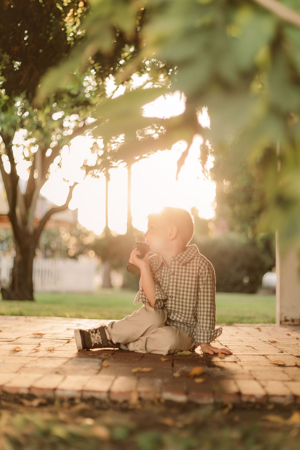 Child sits on brick patio during golden sunset.