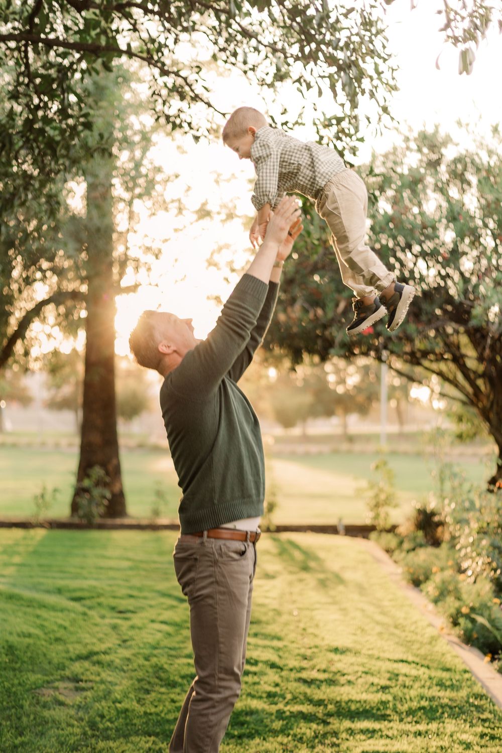 Parent tosses child in air during sunset in grassy park.