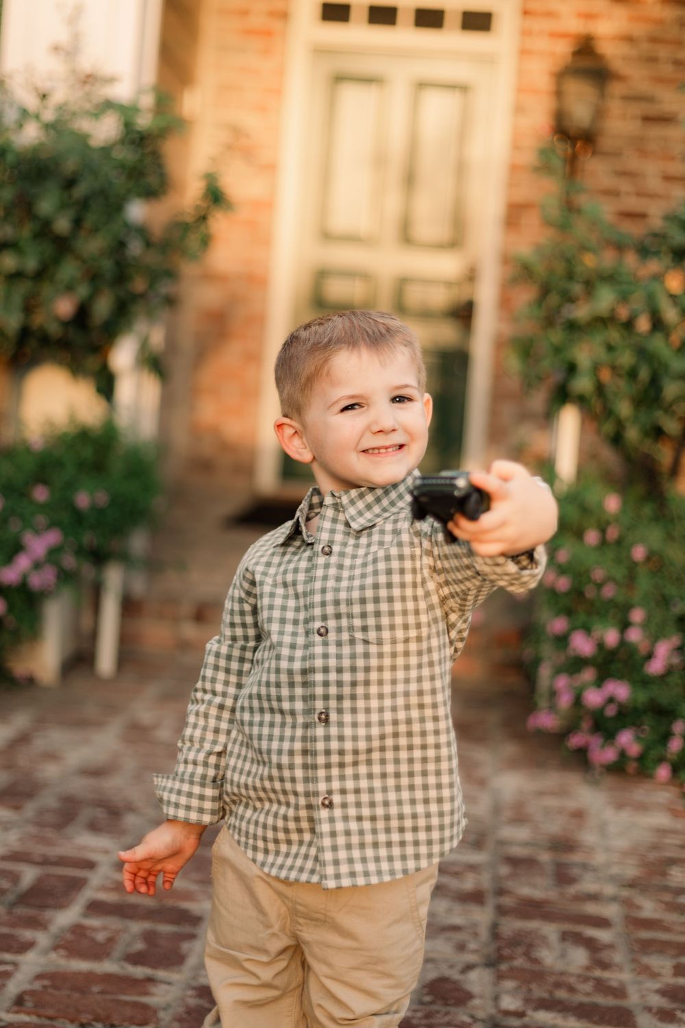 Child in checkered shirt walks on brick pathway near garden.