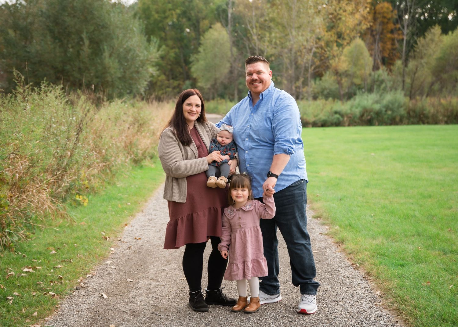 A family walks together on a winding dirt path through a scenic autumn landscape in matching brown and pink outfits.