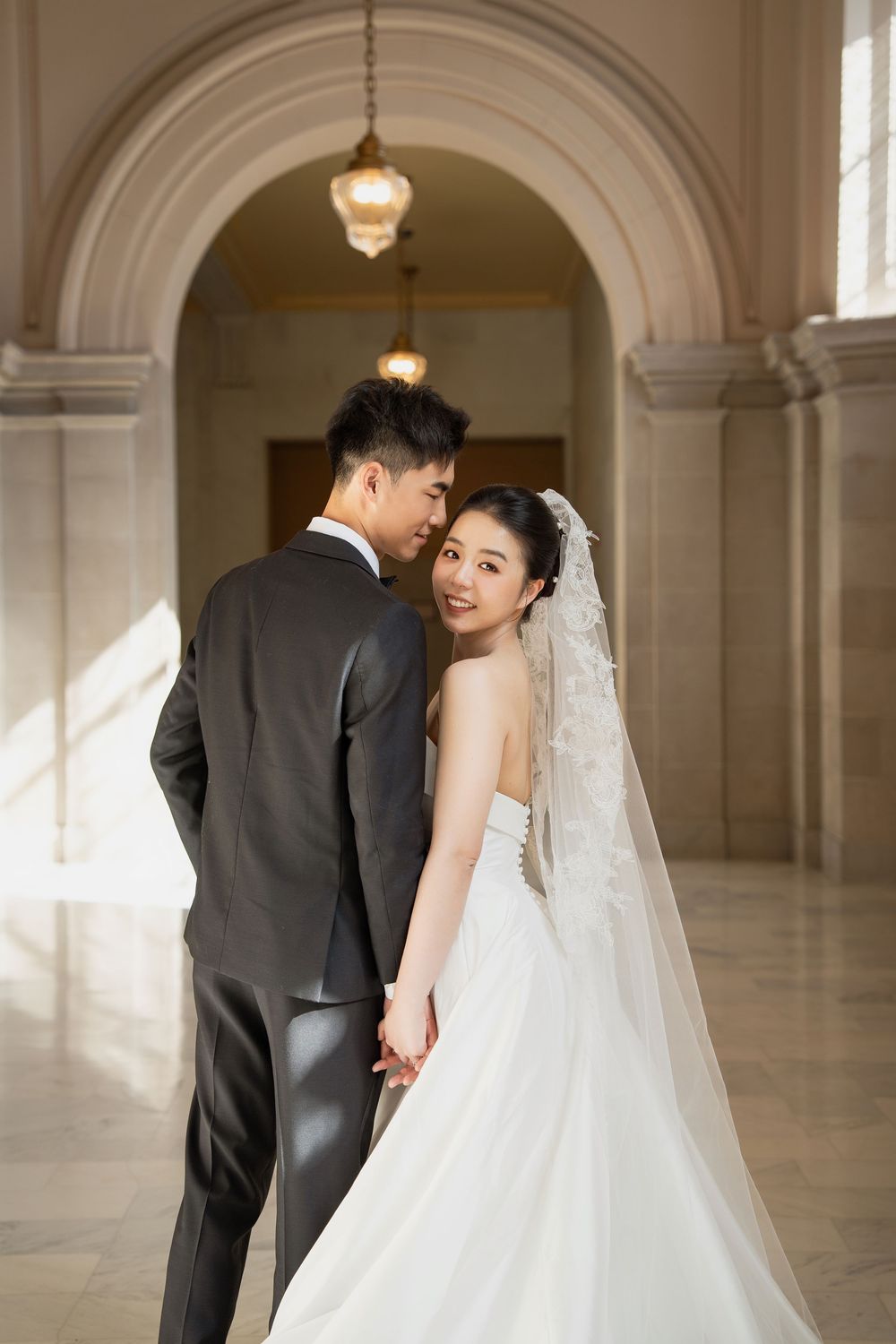 Wedding couple shares intimate moments in a grand marble hallway with arched columns and warm lighting.