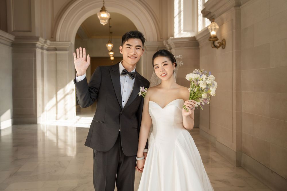 A couple in formal wedding attire poses in an elegant hallway with ornate architecture and warm lighting.