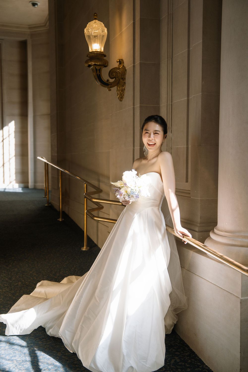 A flowing white wedding dress twirls gracefully in an elegant hallway with ornate wall sconces and columns.