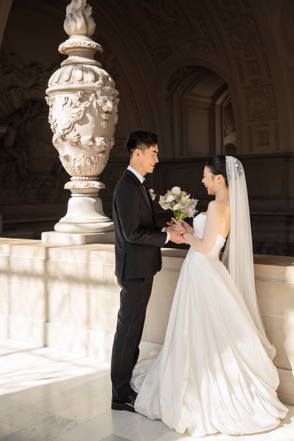 Romantic wedding couple embracing in elegant architectural setting with ornate stone pillars.