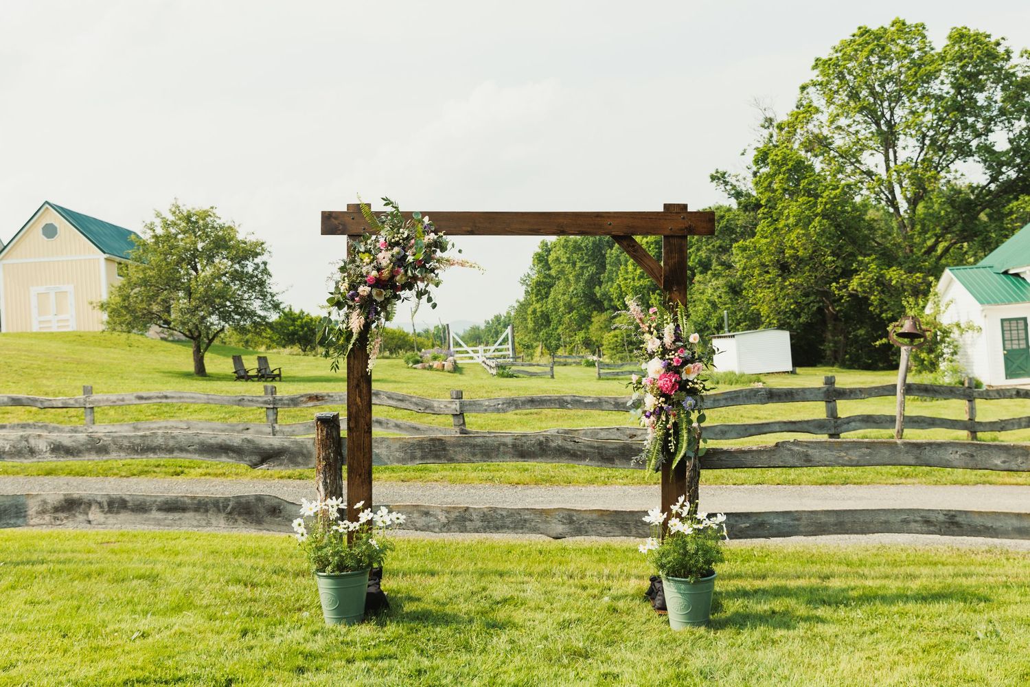 Rustic split-rail fence leads to outdoor wedding venue on rolling green hills.