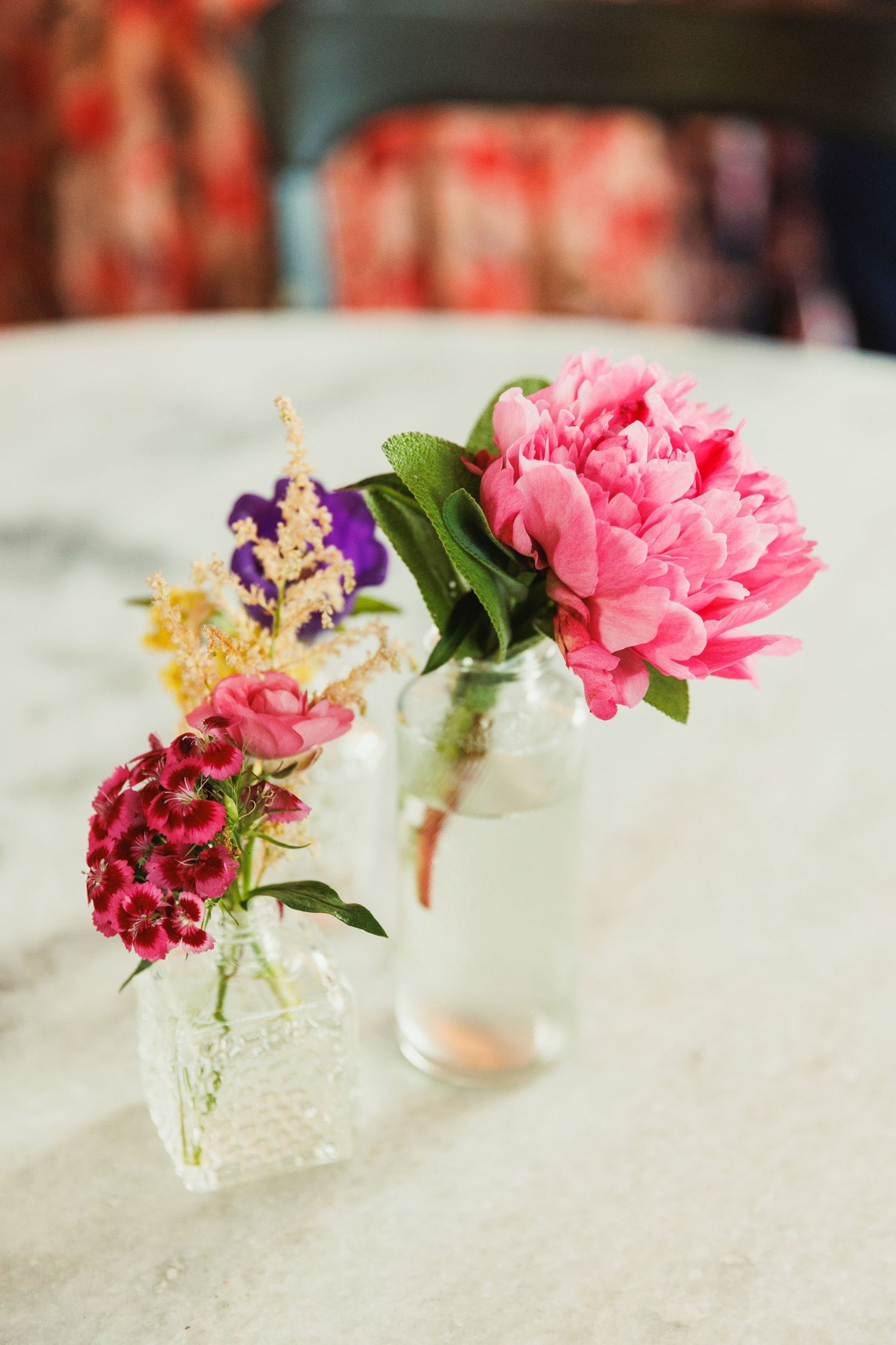 Small crystal vases holding delicate pink and red flowers arranged in a row on a white surface.