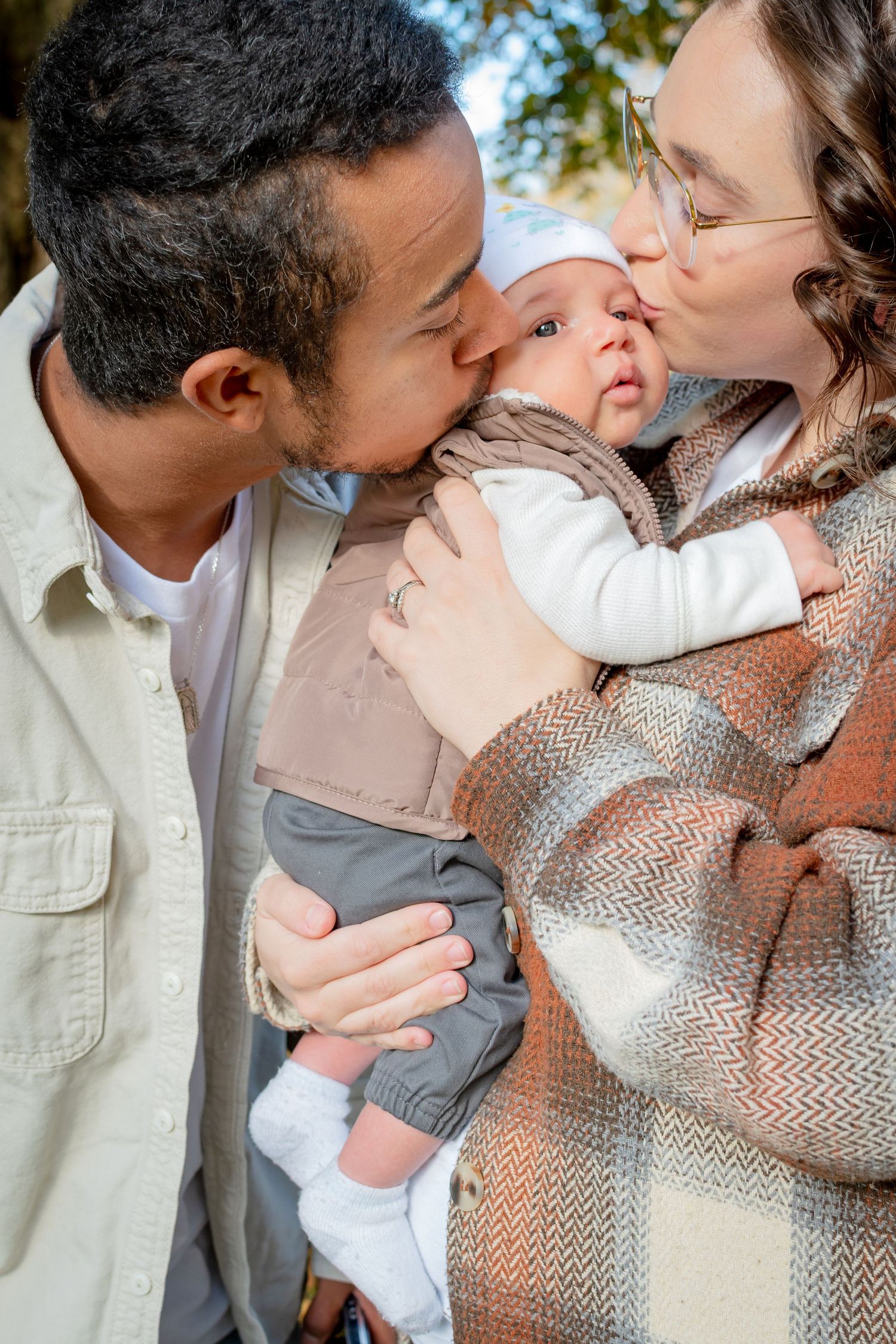New parents kissing their newborn during fall family photos at Wright Park in Tacoma.