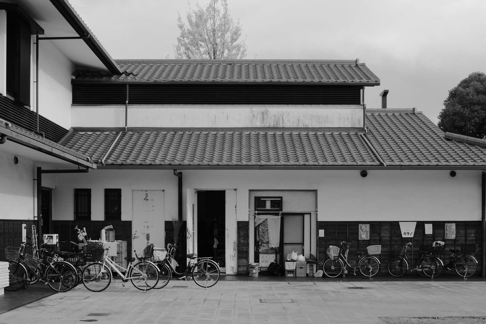 A row of bicycles parked outside a white building with a dark roof on an overcast day.