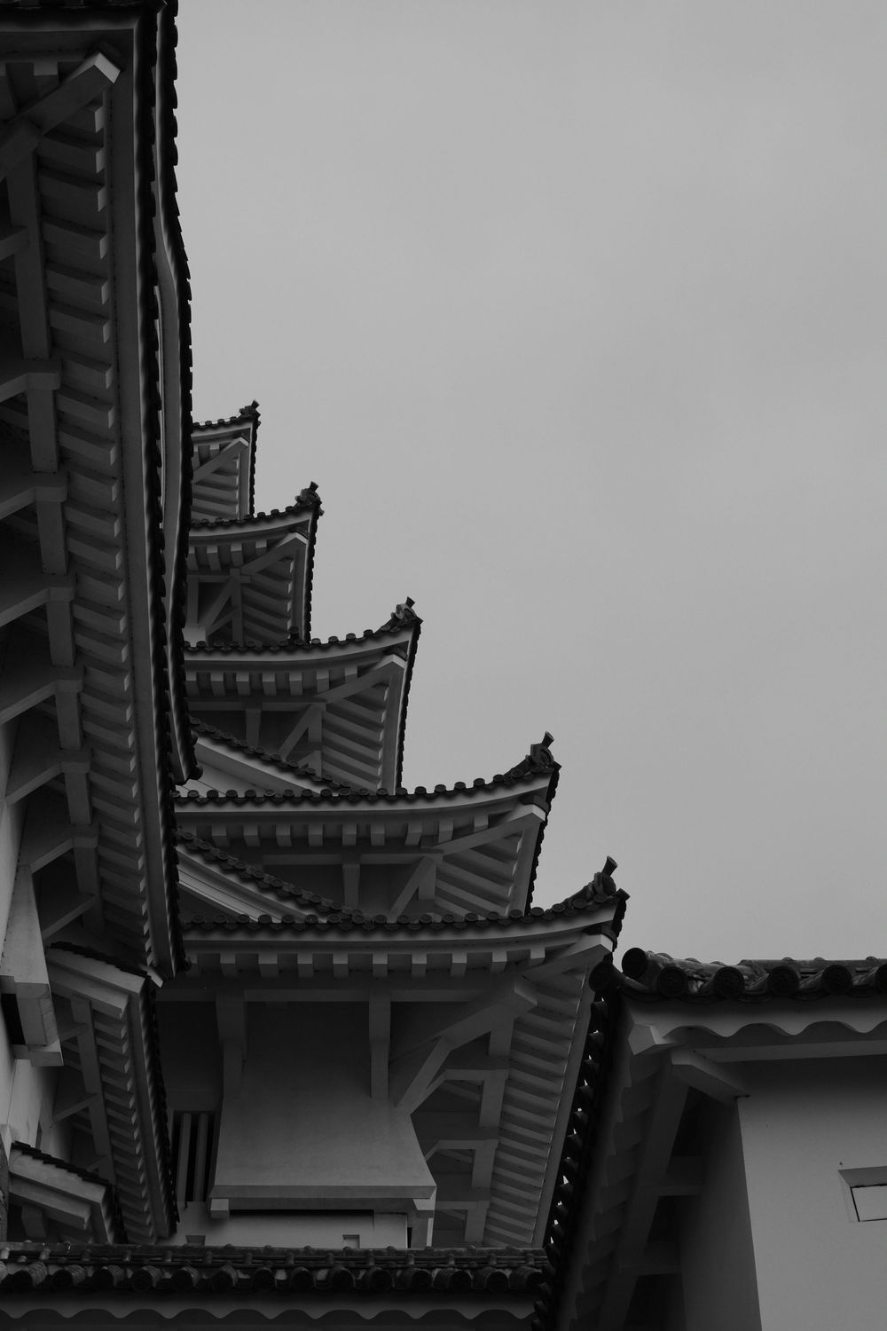 Black and white architectural detail of traditional Asian pagoda rooflines with ornate curved eaves against a cloudy sky.