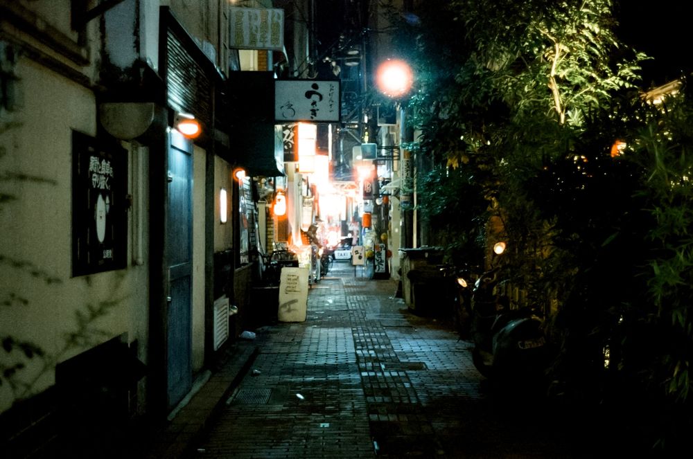 Narrow illuminated alleyways in Japan at night with traditional architecture and glowing lanterns creating ambient light.