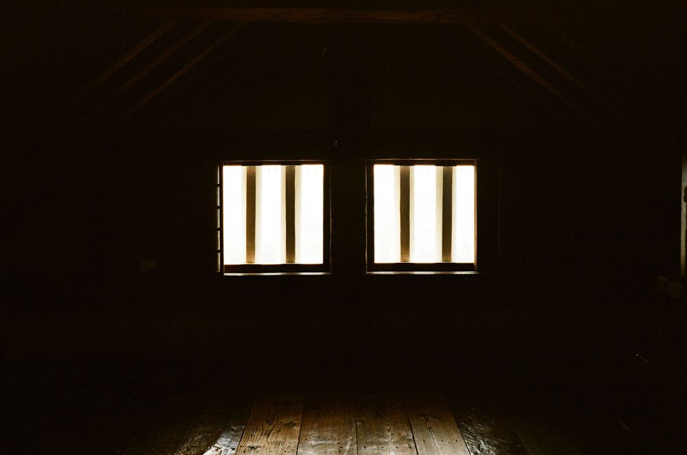 Two glowing windows illuminate a dark attic space with wooden floorboards.