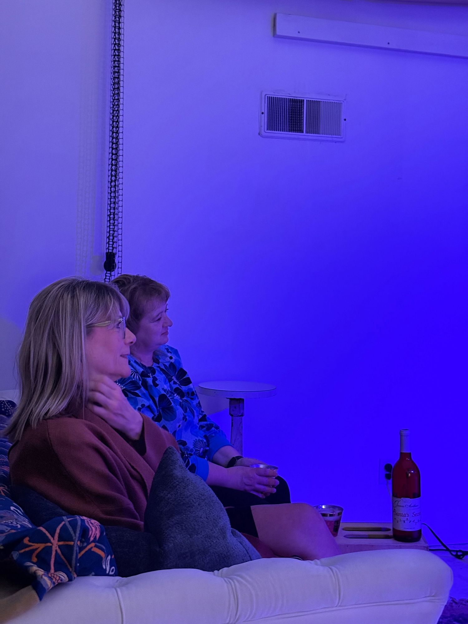 People sit in a dimly lit room with blue ambient lighting creating a moody atmosphere during a presentation.