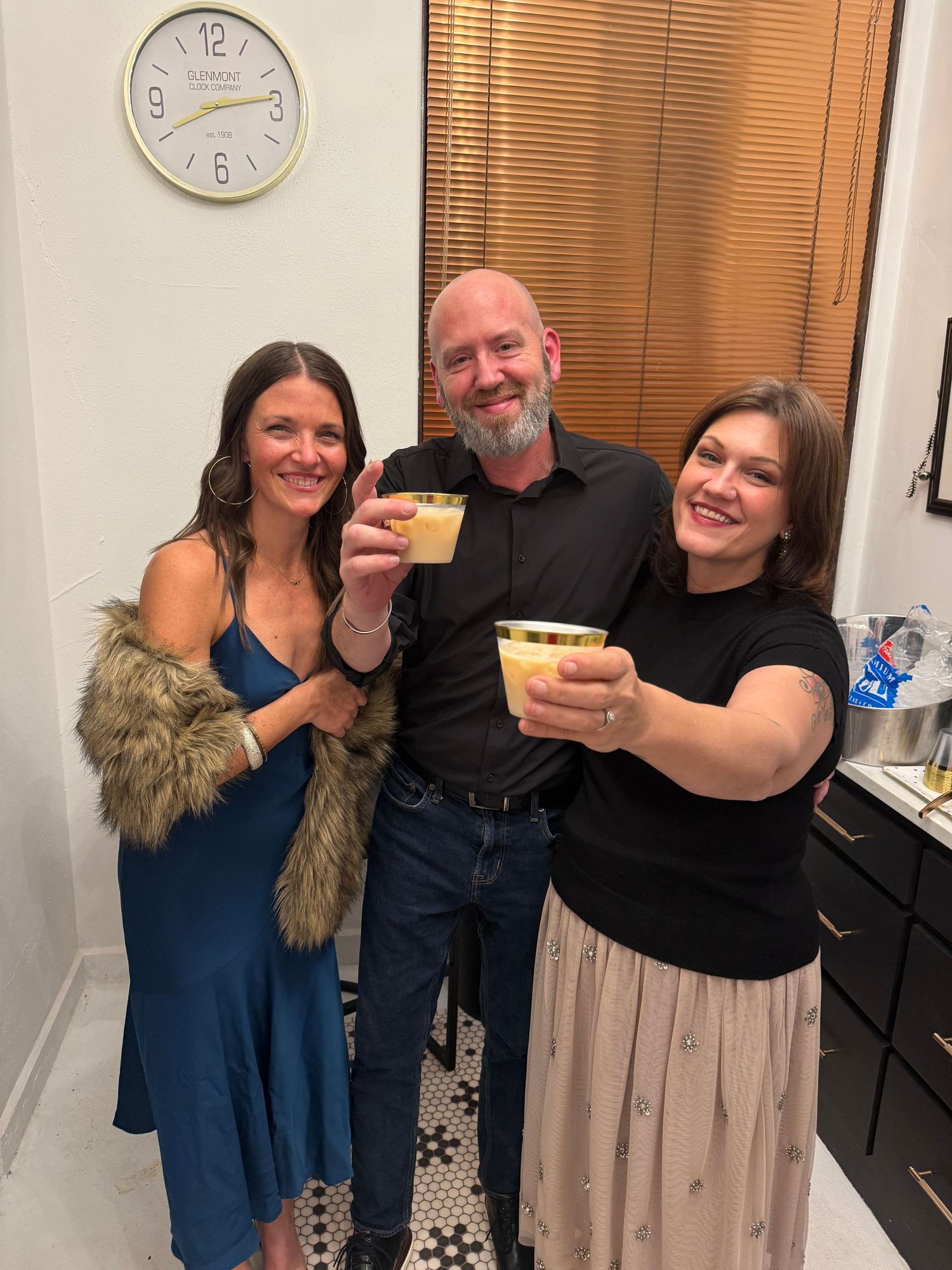 Group of people gathered in a room smiling and celebrating with food and drinks at a casual gathering.