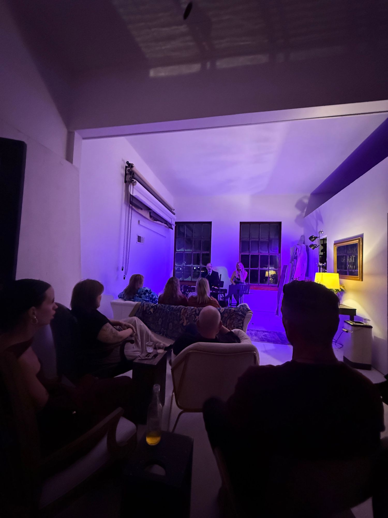 A dimly lit room with purple and blue ambient lighting creates a moody atmosphere during a nighttime gathering.