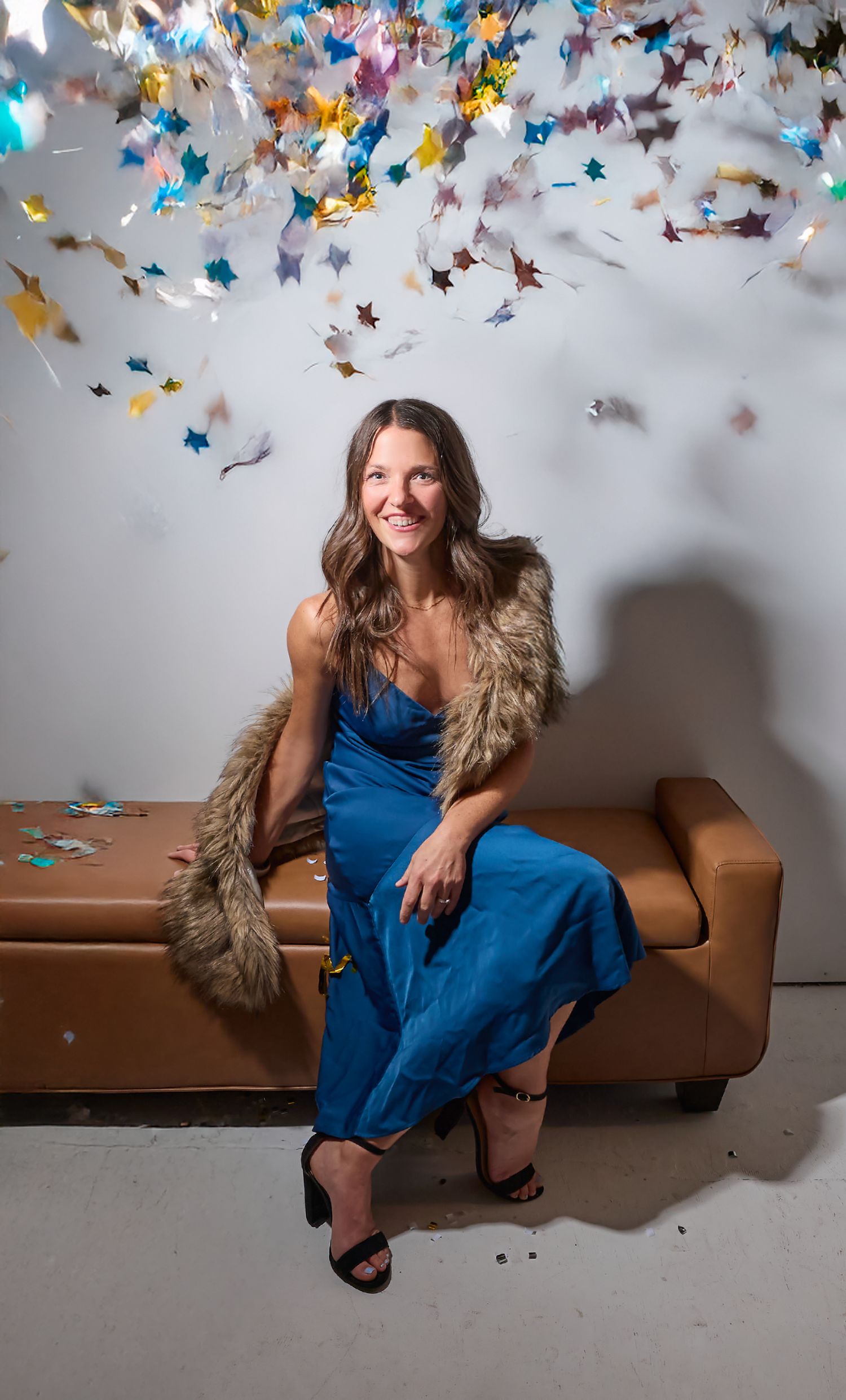 A person in a blue dress sits on a brown couch under colorful paper butterflies suspended from the ceiling.
