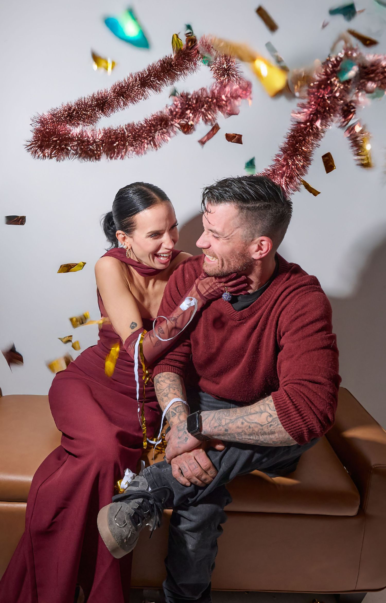 A couple shares a joyful moment on a couch with pink tinsel and confetti falling around them in a celebratory setting.