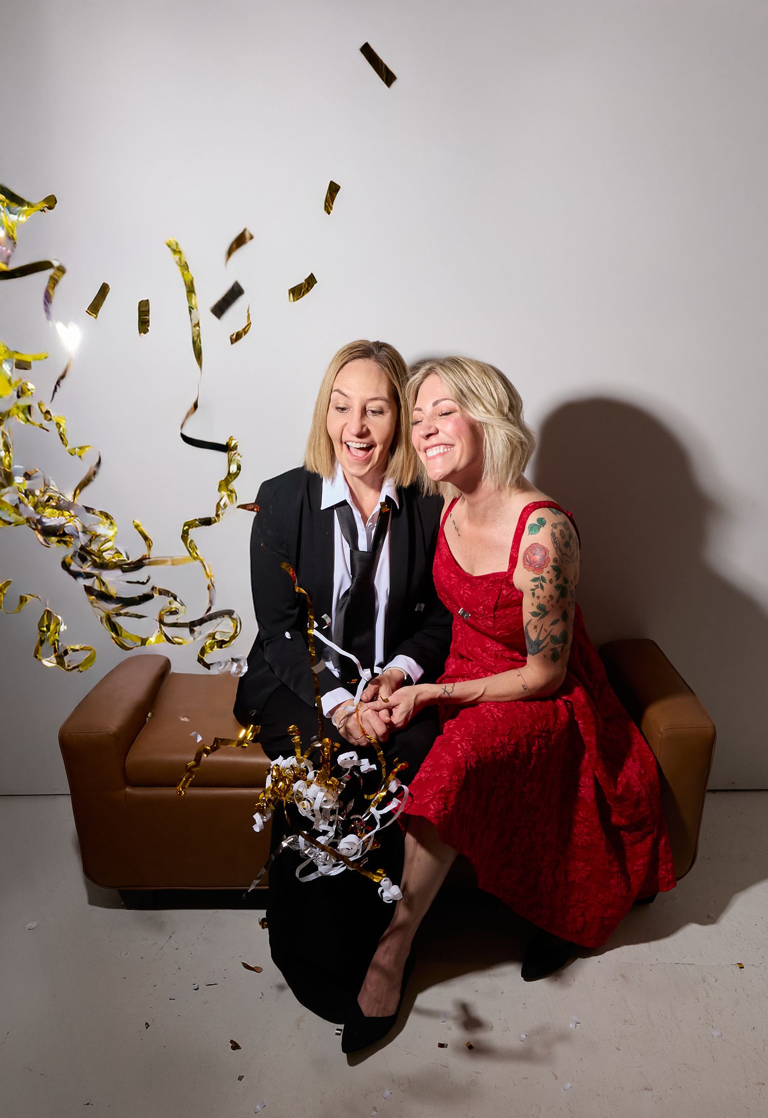 Two people in formal attire laugh together on a brown couch as gold confetti falls around them in a photo series.