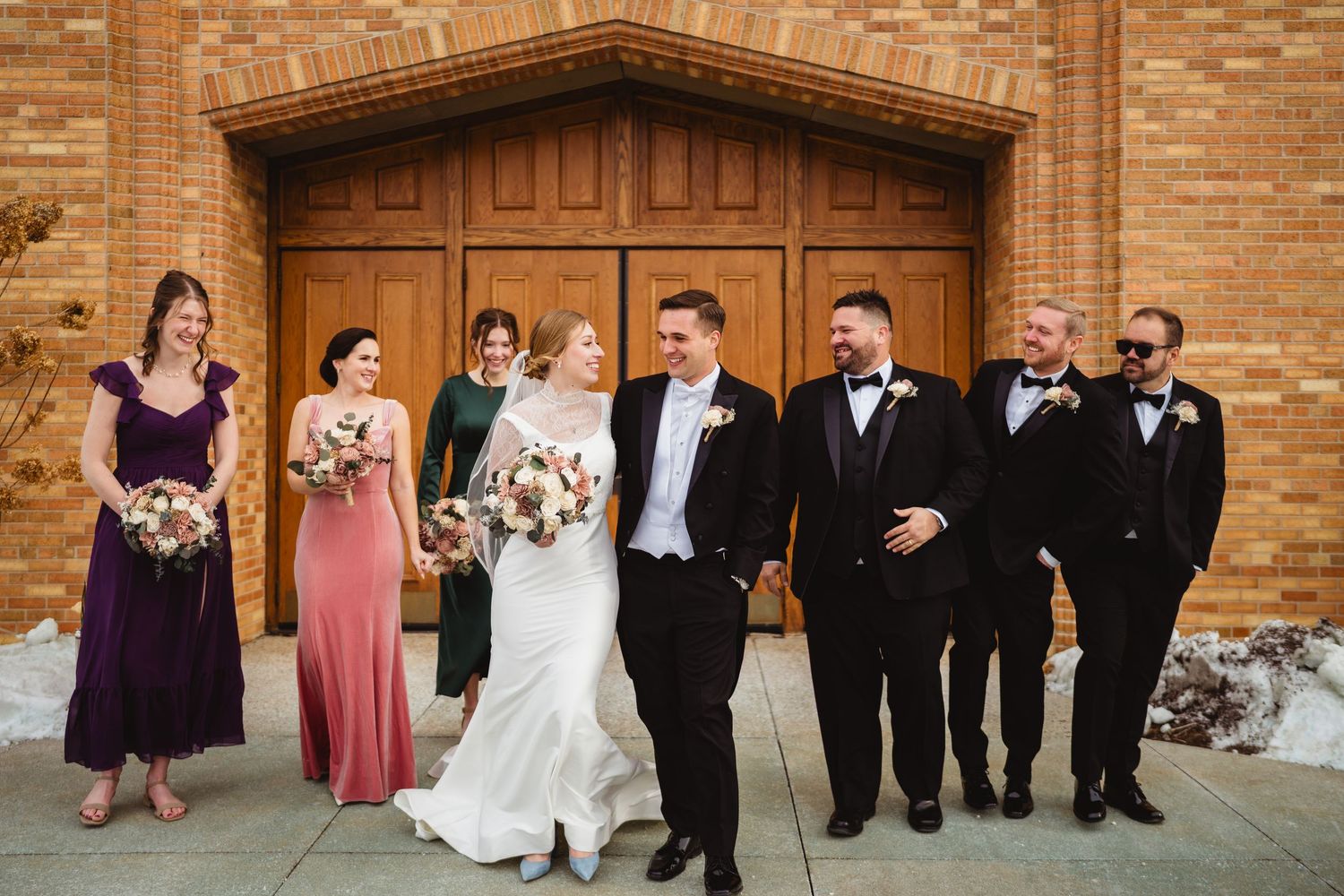Wedding party members lined up in formal attire against a brick wall at a church venue.