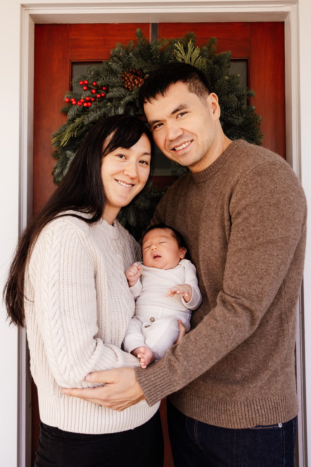 Parents hold their new baby in front of their Christmas wreath at their San Jose home