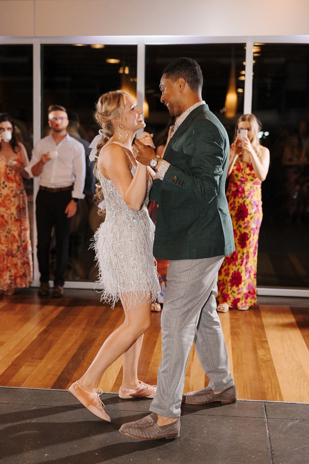A couple dances together at a wedding reception, with the woman wearing a sparkly white fringe dress and the man in a green blazer.