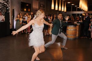Couple performs an energetic dance move at a wedding reception with guests watching in the background.
