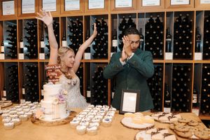 Wine bottles line the walls of a cellar while people gather around a table with desserts and appetizers.