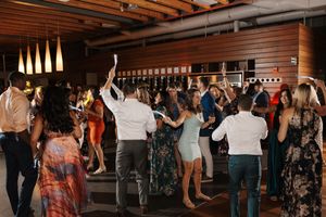 A large group of people dancing with raised hands at an indoor venue with wooden beams on the ceiling.