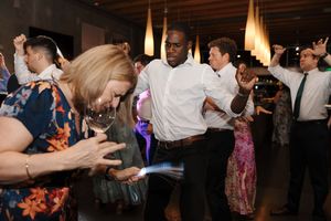 A group of people dancing and celebrating together at a lively party or reception with warm lighting.