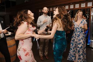 People dancing and enjoying themselves at a lively indoor wedding reception with wooden ceiling beams visible.