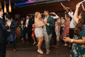 Party guests dancing in a dimly lit venue with purple and blue lighting creating a festive atmosphere.