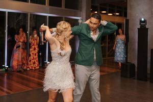 Wedding guests dance together on a dimly lit dance floor during an evening reception celebration.