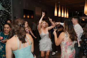 Wedding guests dancing and celebrating on a crowded dance floor at a reception party with colorful lighting.