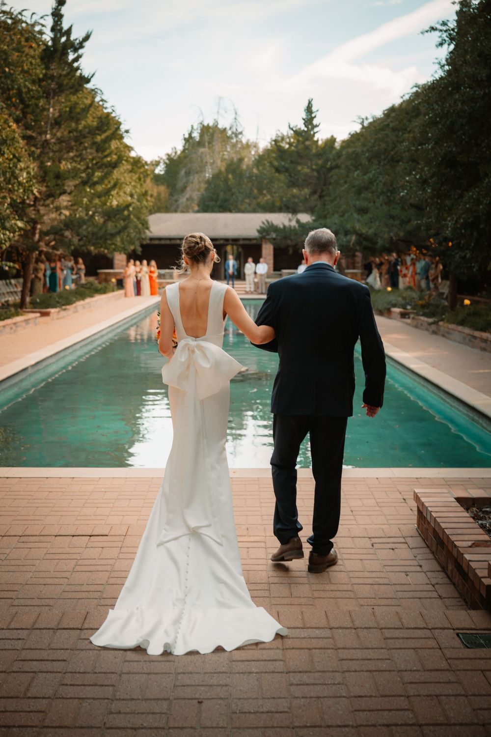 Sheath style wedding dress on bride walking down the aisle at Clark Gardens in Weatherford, Texas. Wedding ceremony in Bridgerton setting.