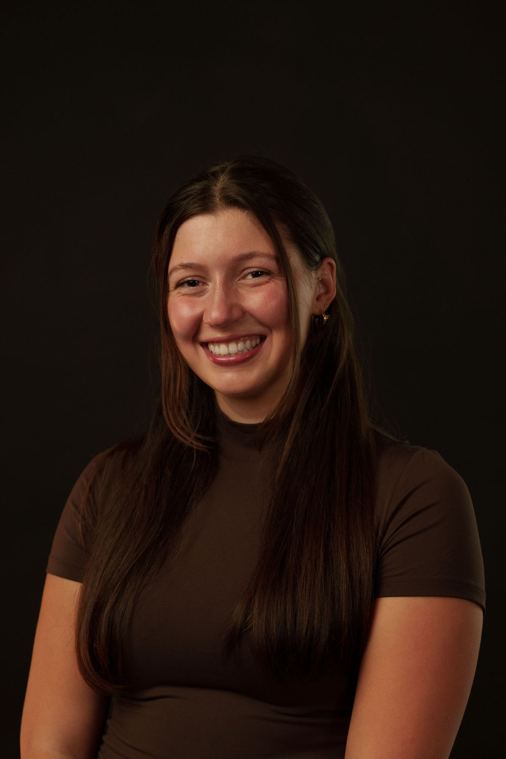 Portrait against a dark background shows someone wearing a brown turtleneck top and smiling warmly.