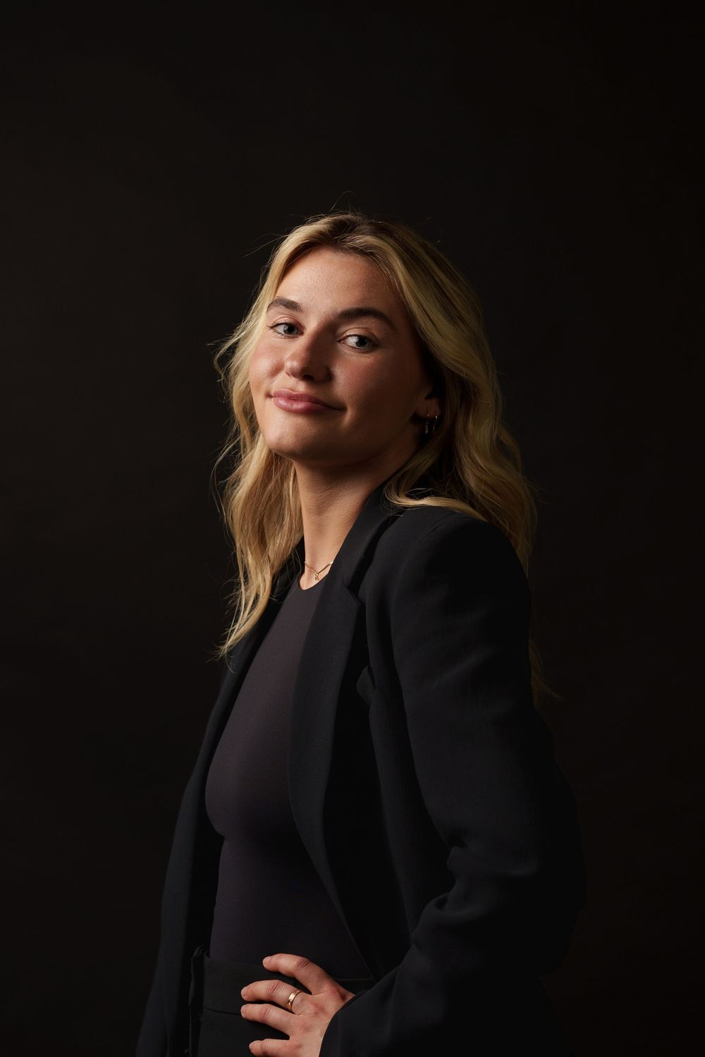 Professional studio portrait of a person in business attire against a dark background with dramatic lighting.