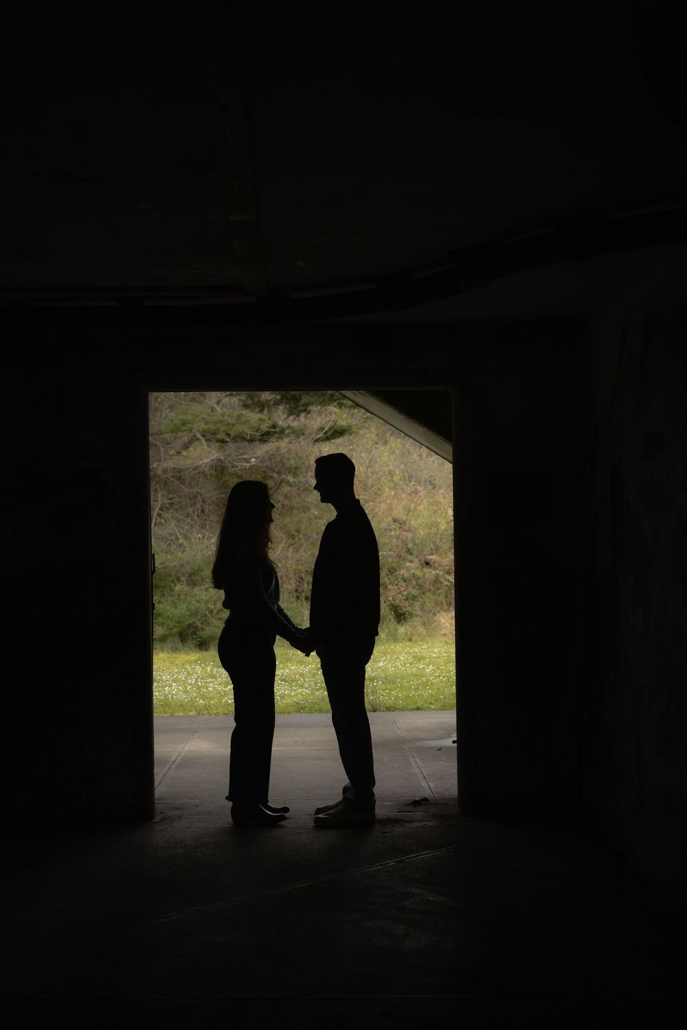 Two silhouettes standing and facing each other in a dark tunnel with bright daylight visible through the opening.
