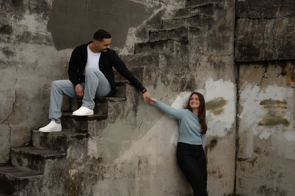 Two people having fun on concrete steps outdoors with one reaching down to help the other up.