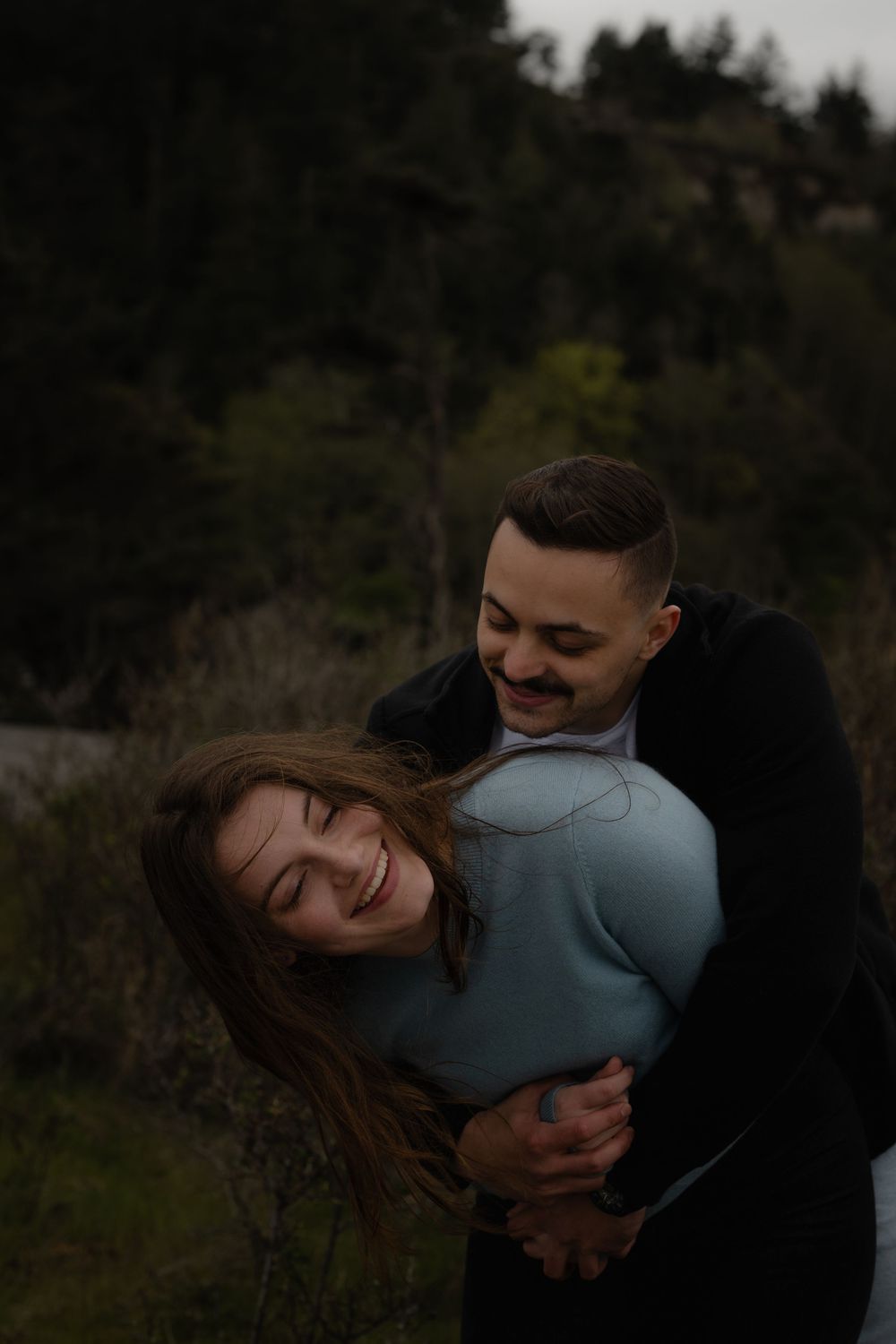 A couple embraces and shares joyful laughter together during an intimate outdoor photoshoot in a natural setting.