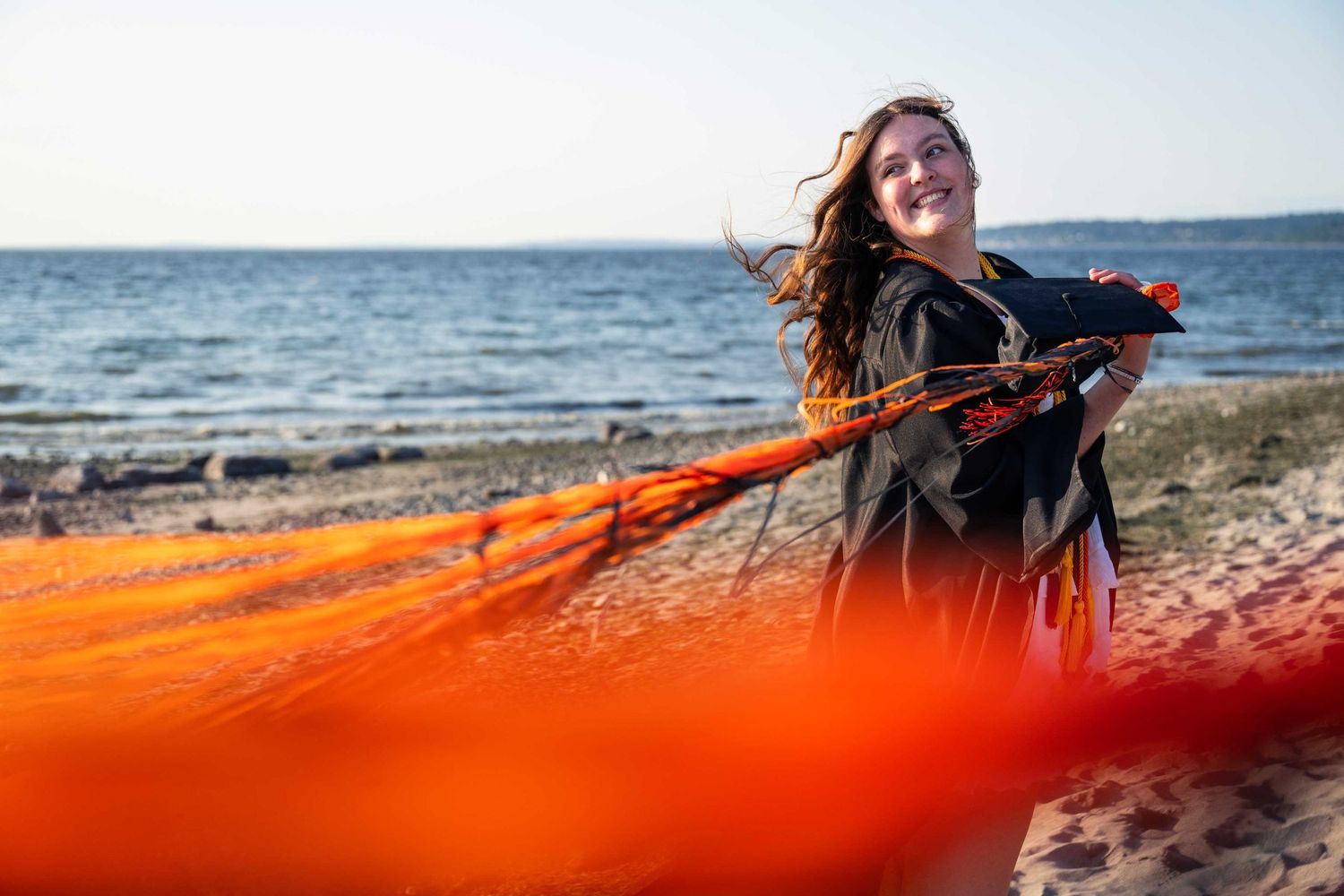 Orange flowing fabric creates dynamic motion against a coastal beach backdrop on a sunny day.