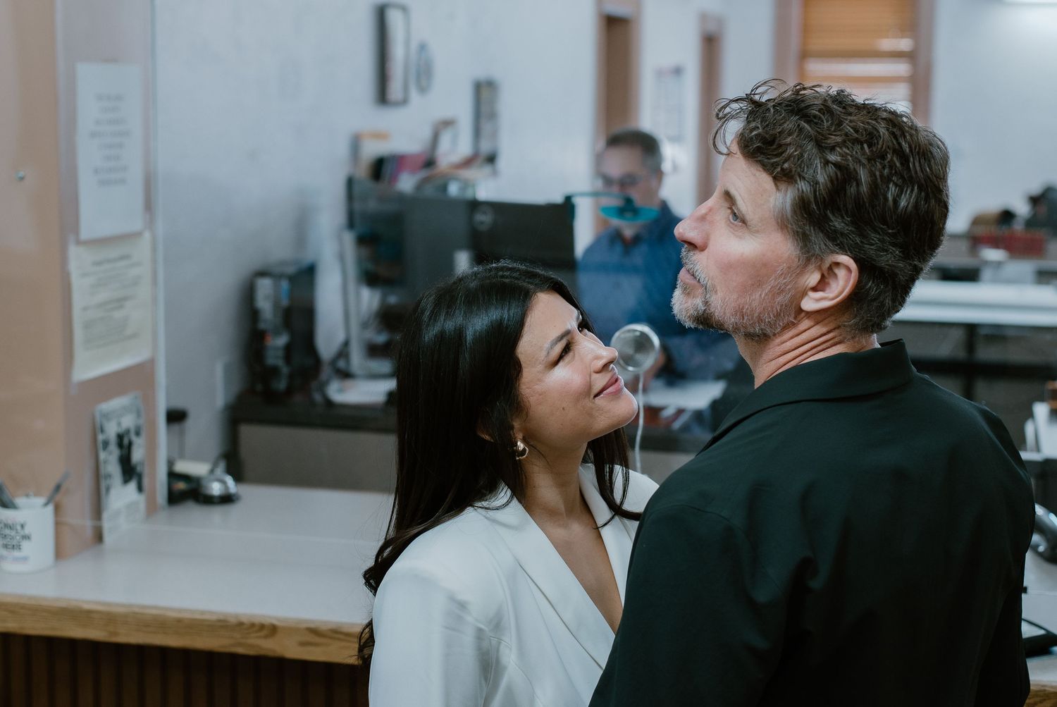 A couple shares an intimate moment at a government office counter, with staff visible in the background.