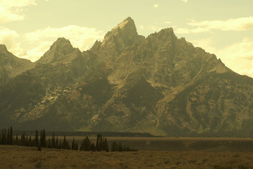 A panoramic view of the majestic Grand Teton mountain range at sunset with golden light illuminating the rugged peaks.