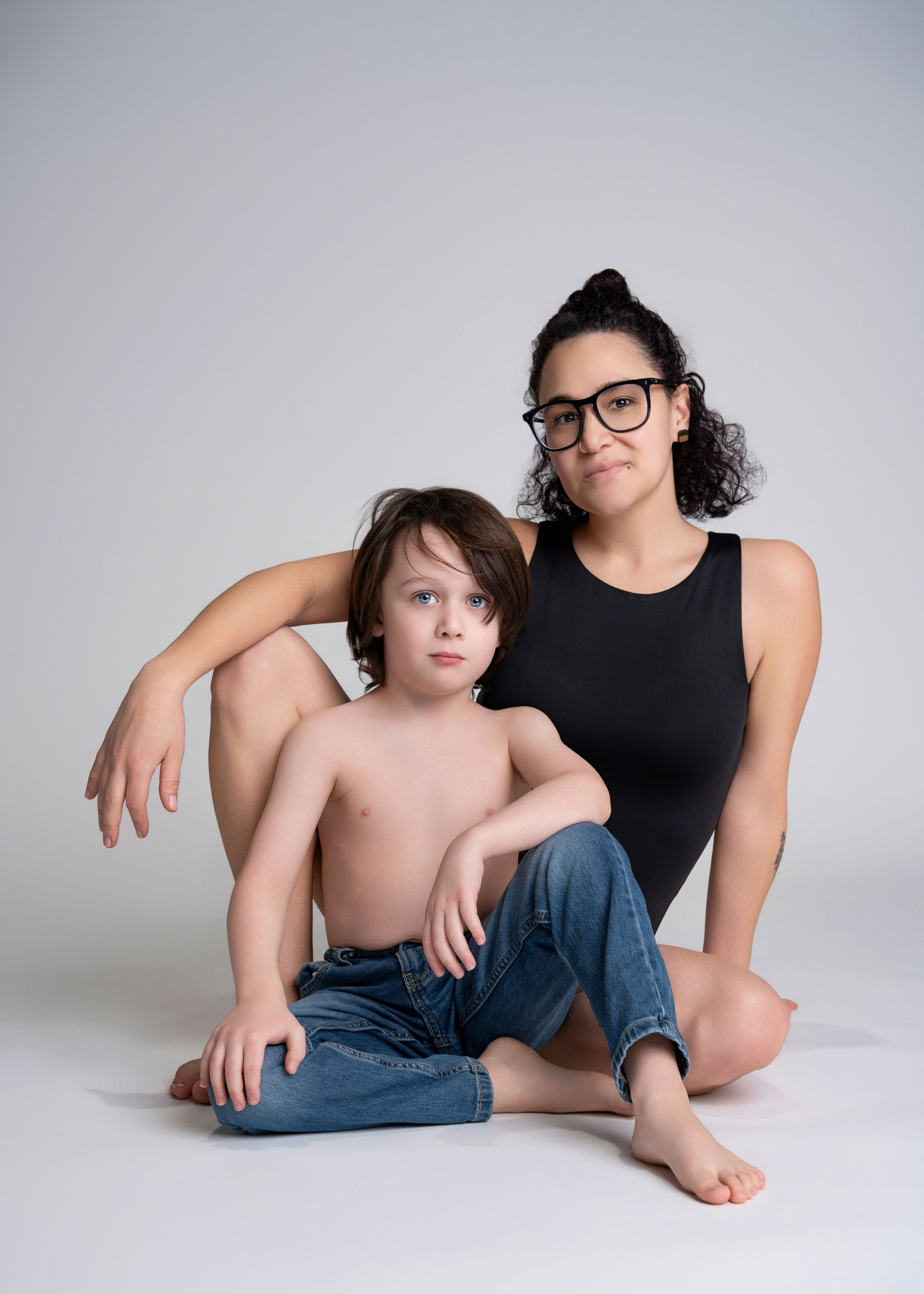 a woman sits behind her son in the studio with a motherhood photographer
