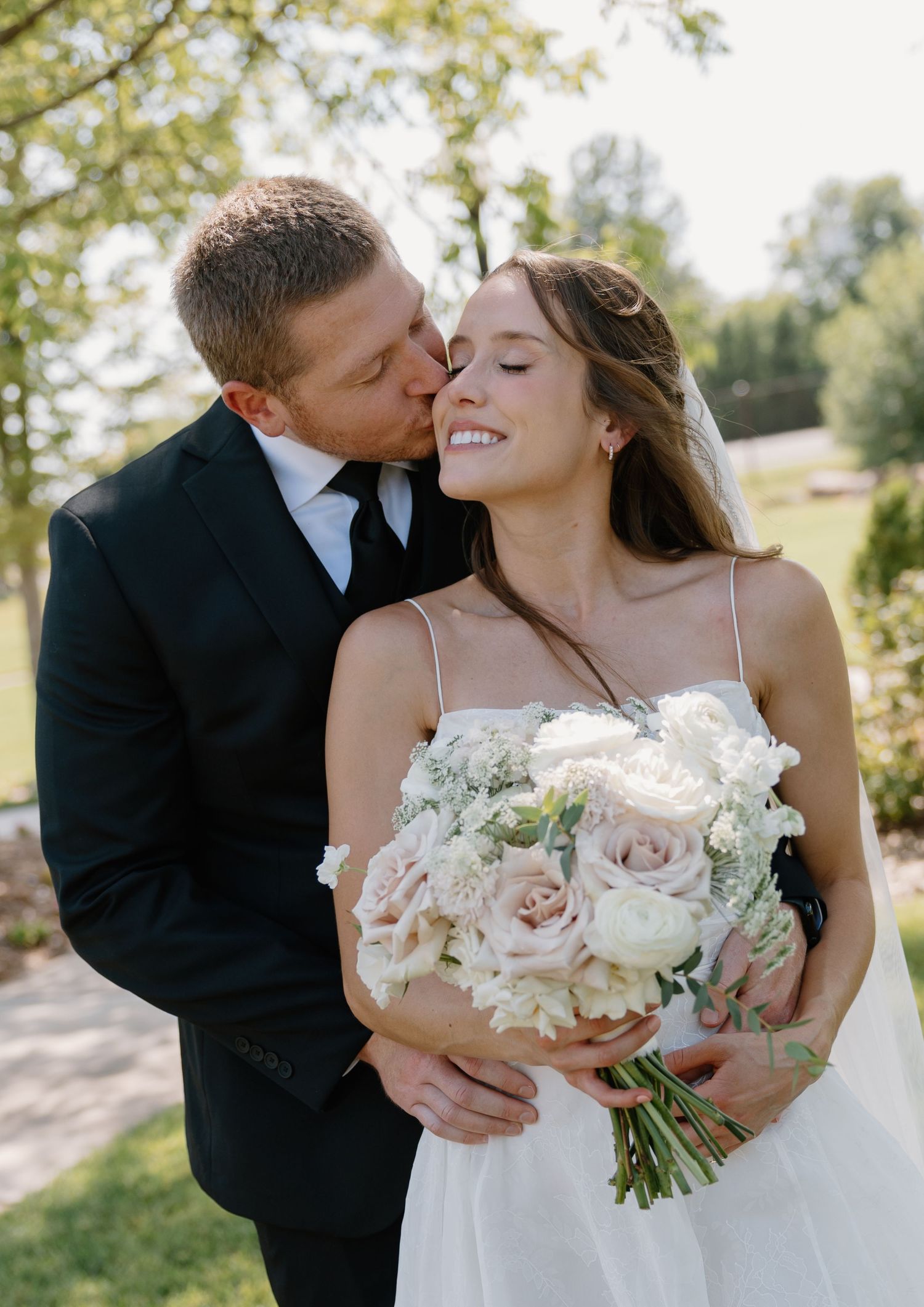 A romantic sunset wedding photo of a couple embracing on a manicured lawn in front of an elegant mansion estate.