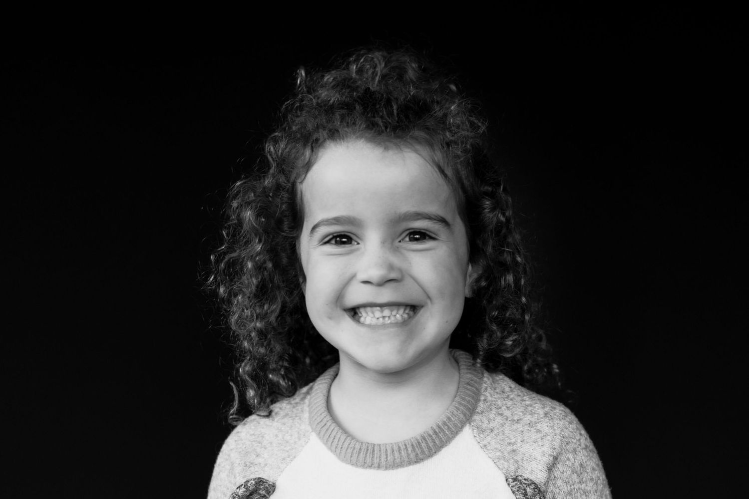 Cheerful young girl with curly dark hair laughing, wearing a white raglan shirt in black and white photo.