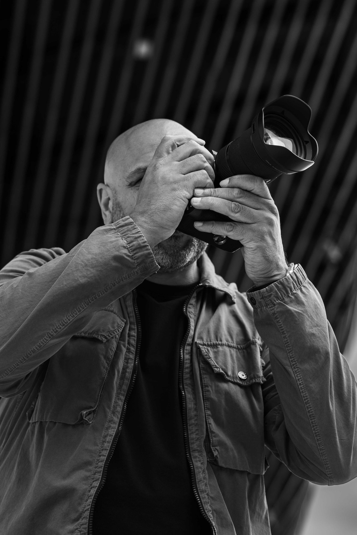 Black and white photo of a photographer in a jacket holding a camera up to his face while taking pictures.