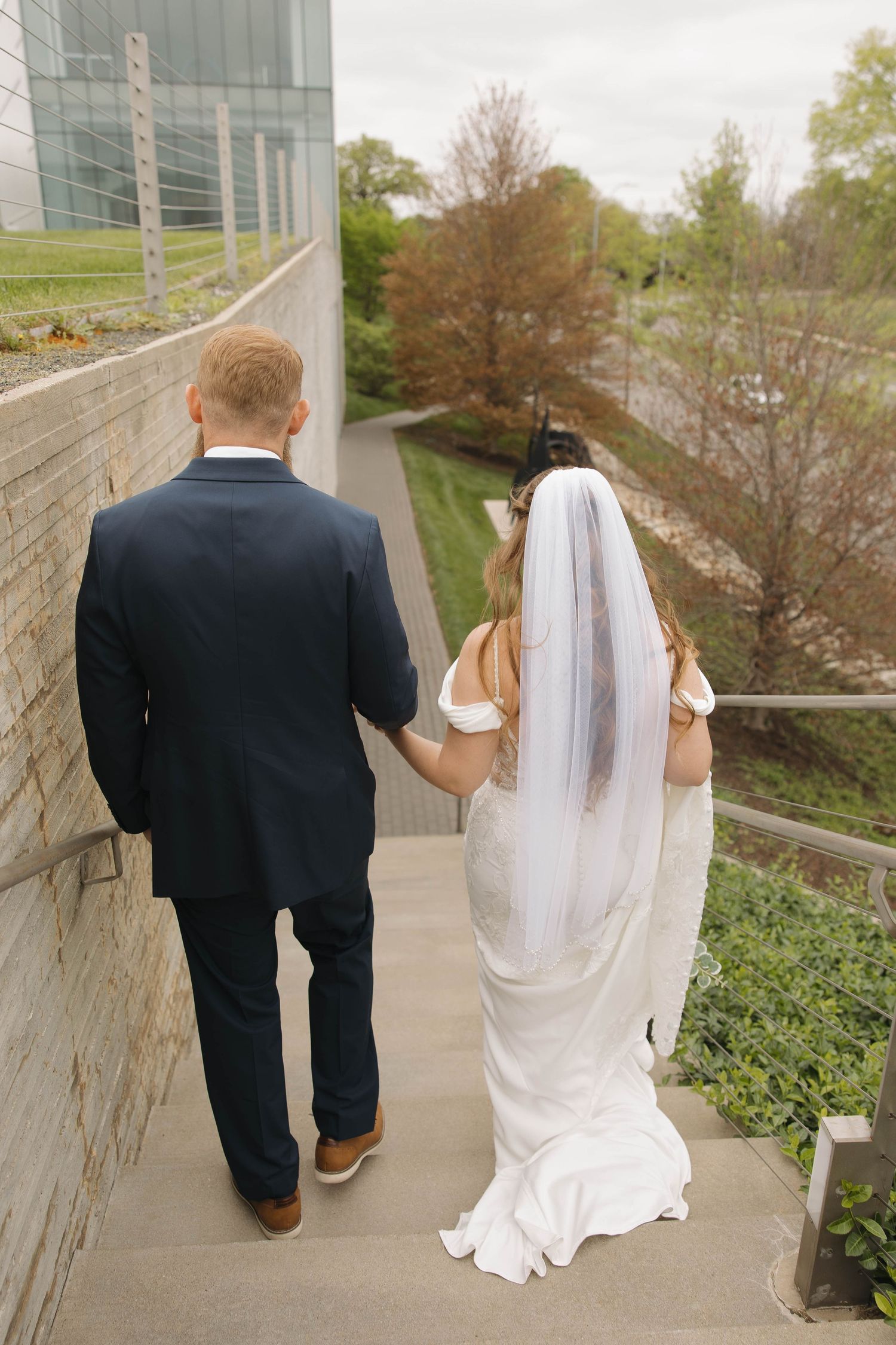 Newlyweds walk down outdoor steps together with the bride in a flowing white dress and veil at the Nelson Atkins in Kansas City, Mo.