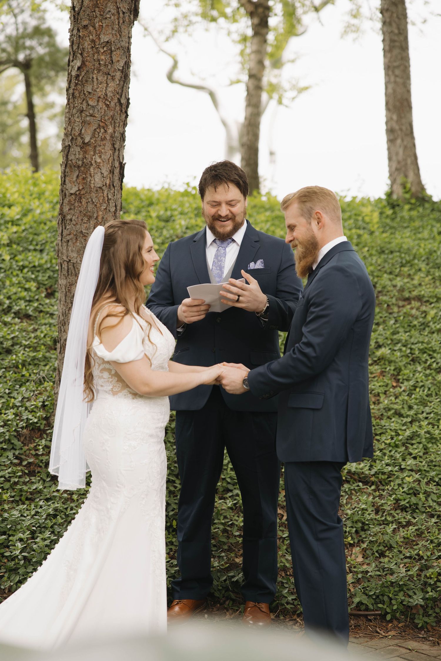 An outdoor wedding ceremony taking place in a wooded setting with an officiant and couple at the altar.