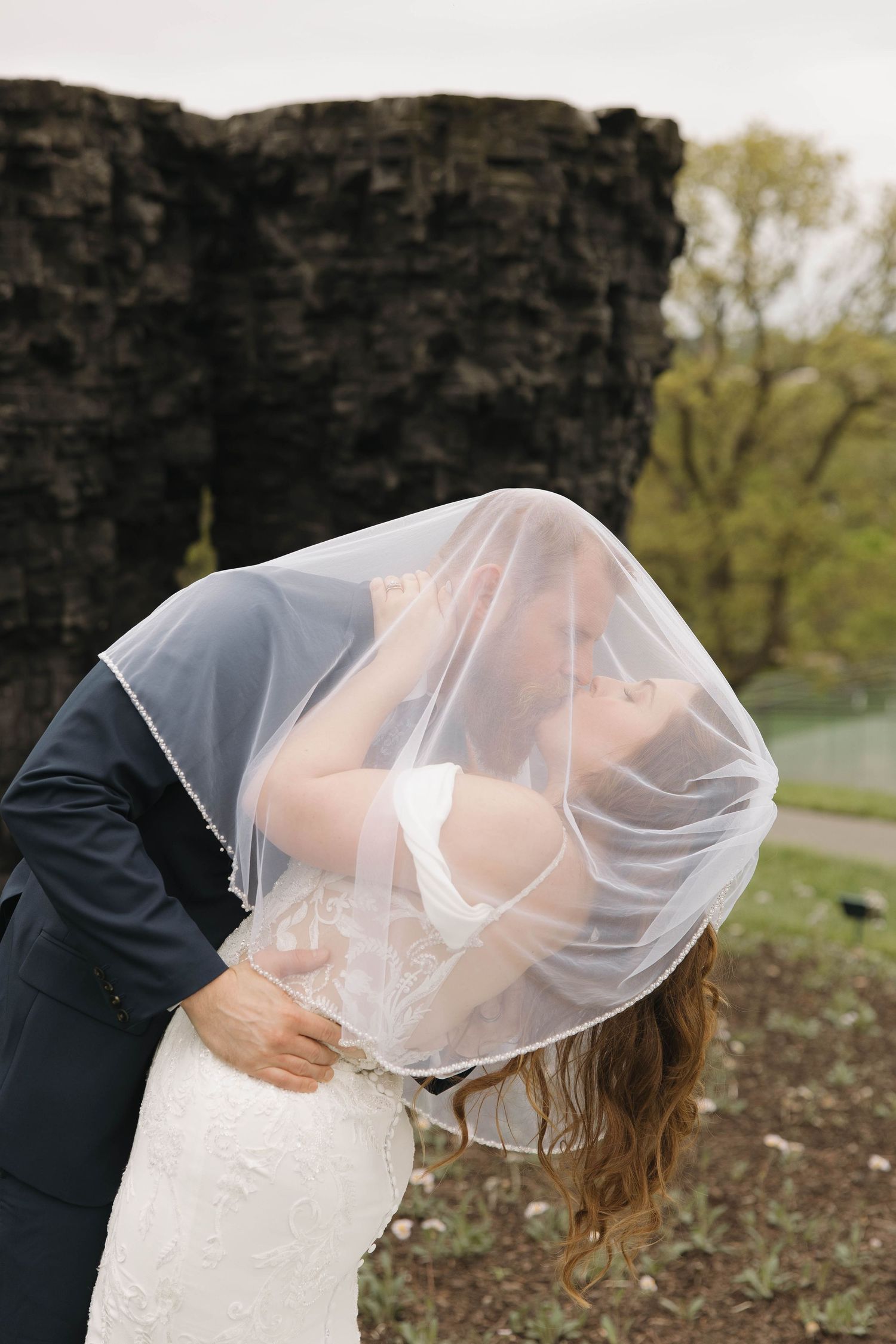 A romantic dip kiss between newlyweds with the bride's veil flowing during their wedding photos.