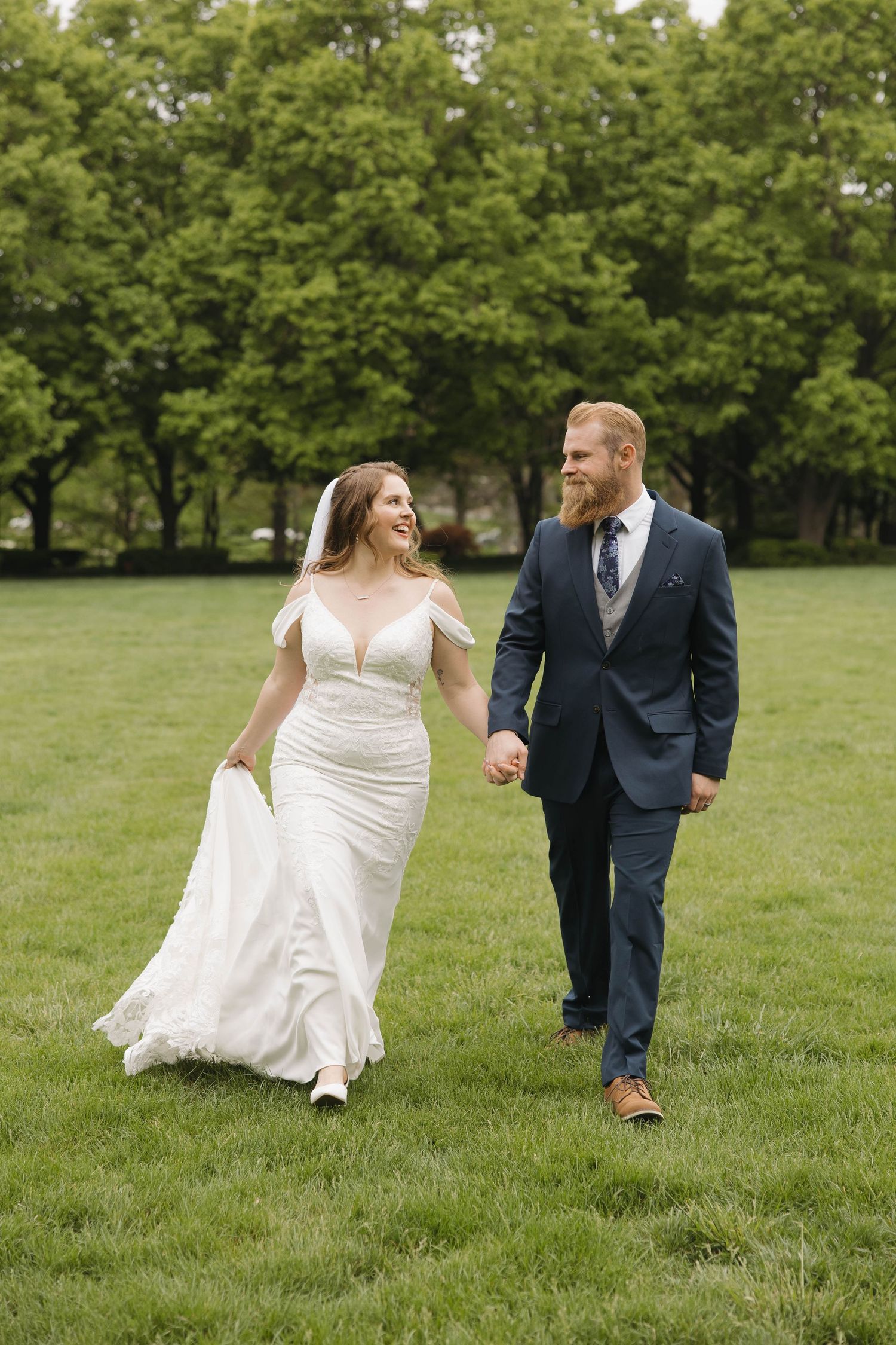 Happy couple walks together on lush green lawn during their wedding day photoshoot.